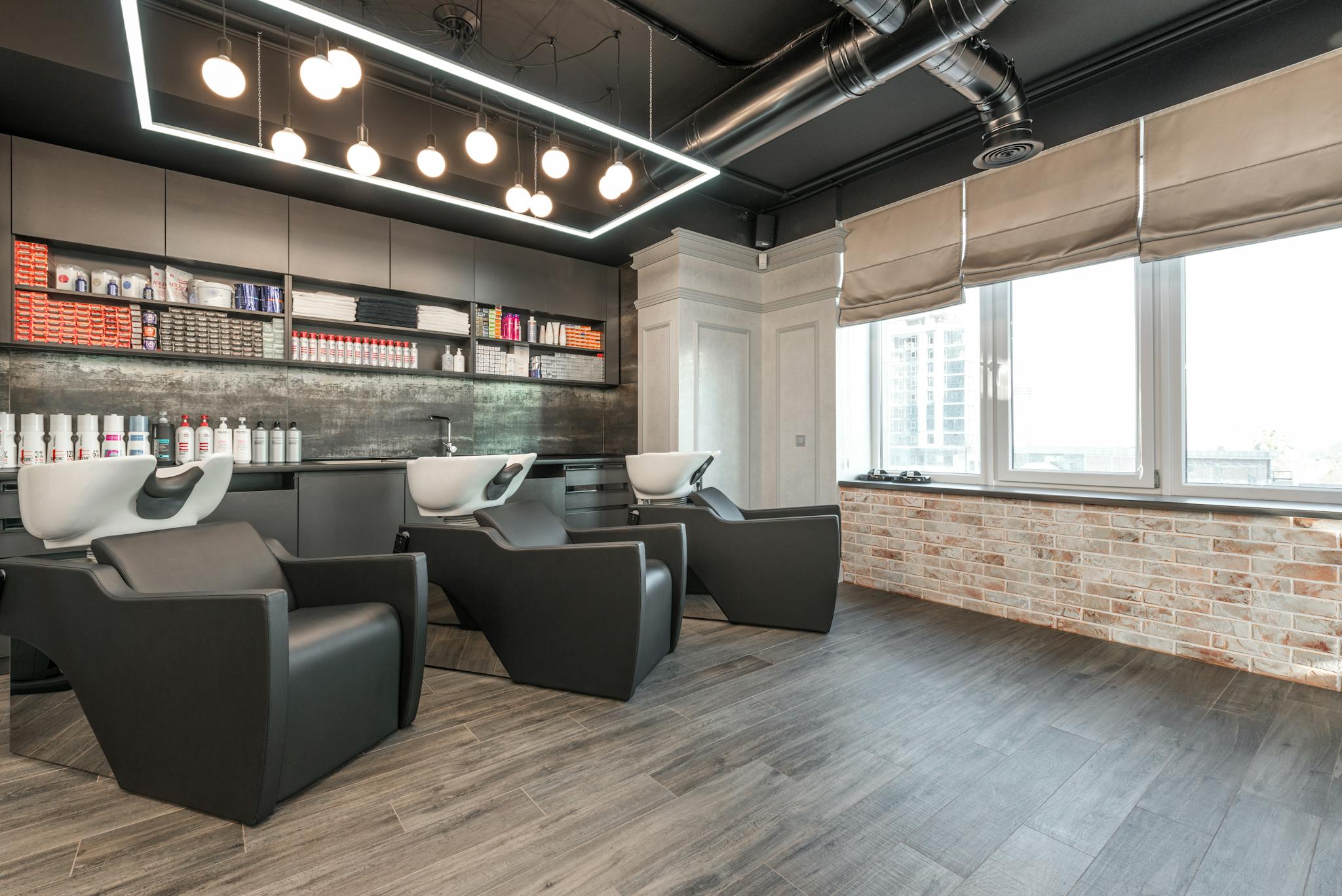Modern leather chairs with backwash sinks placed in modern spacious beauty salon with windows and various professional supplies under glowing lamps